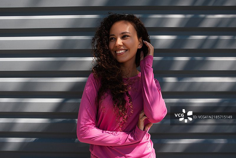 穿着运动服的深肤色女性肖像。美丽的深肤色女孩在街上。健康的生活方式。深肤色女性在街道旁的墙壁附近的肖像。图片素材