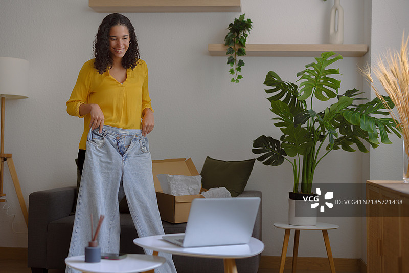 兴奋的年轻女性在家中视频通话时展示新牛仔裤图片素材