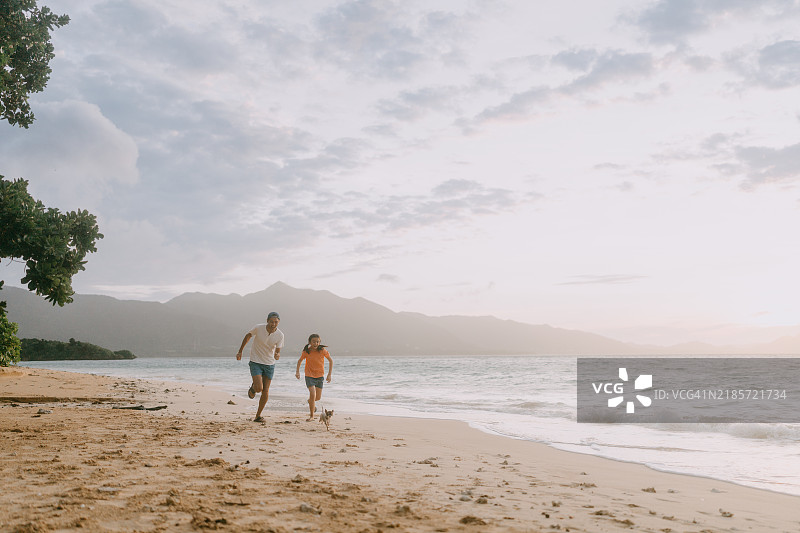 父亲和孩子在日落时分的海滩上与狗一起奔跑图片素材