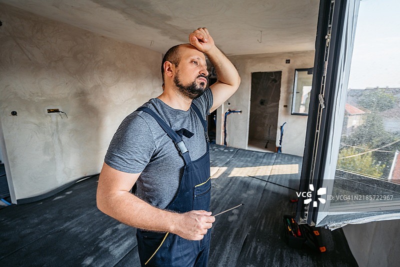 修理工在空置的正在装修的公寓里拧窗户时感到疲惫图片素材