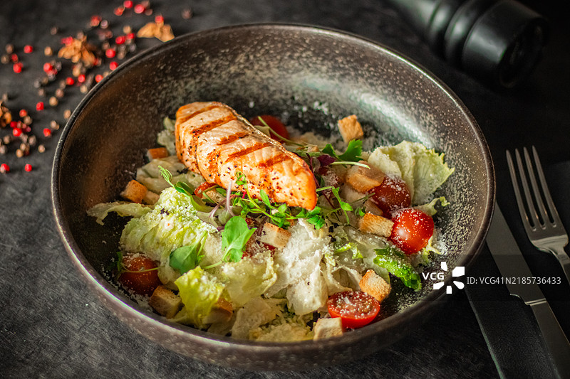 一个碗里的沙拉，上面放着烤三文鱼片、樱桃番茄、面包丁和磨碎的奶酪。图片素材