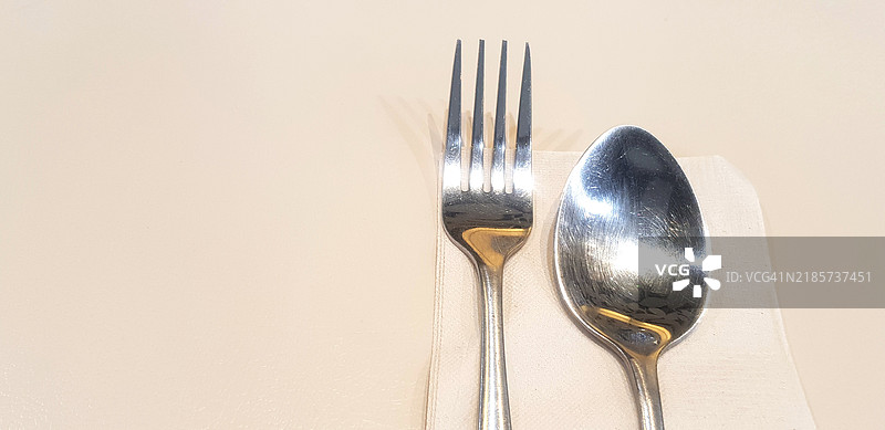 不锈钢叉和勺子放在棕色餐巾或纸巾上，摆放在有空位的餐桌上图片素材