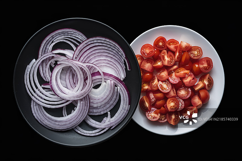 一张两盘食物的照片，一盘上放着切好的红甜洋葱，另一盘上放着切丁的番茄。图片素材