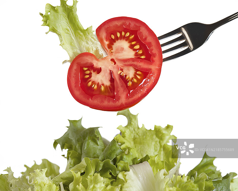 一片切好的番茄，鲜红的果肉和可见的种子，被一把银色叉子高高举起。图片素材