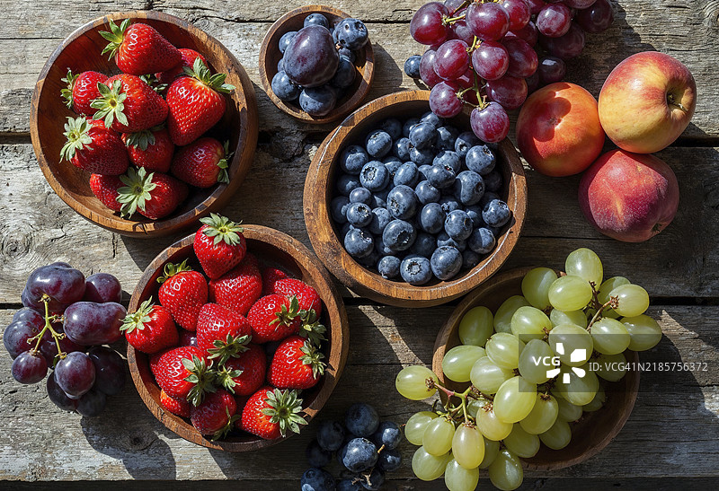 各种新鲜水果拼贴在乡村风格的木碗中，摆放在木质表面上图片素材