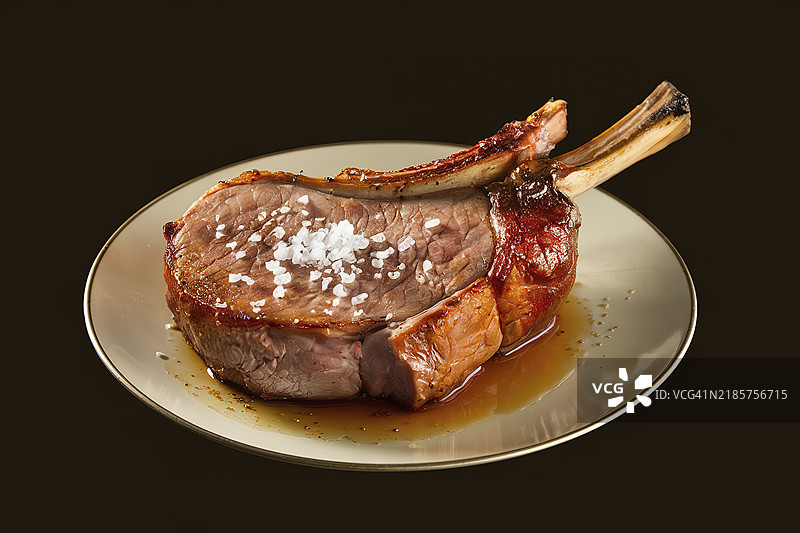 一块烟熏猪排放在盘子里，背景为黑色。图片素材