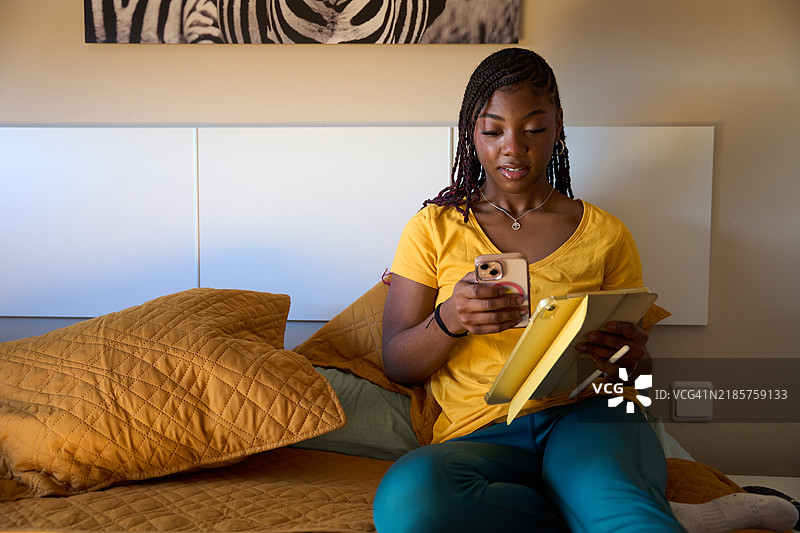 年轻女性在床上使用智能手机和平板电脑图片素材