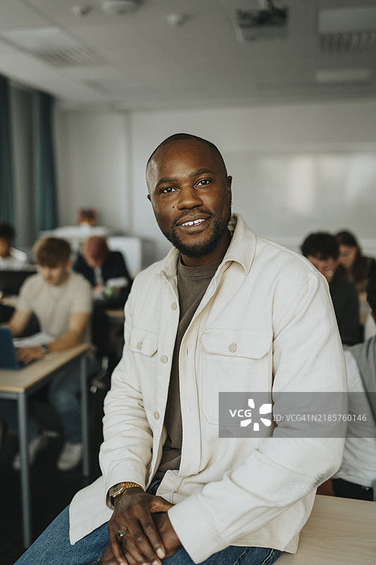 微笑的男教师坐在高中教室的桌子上图片素材