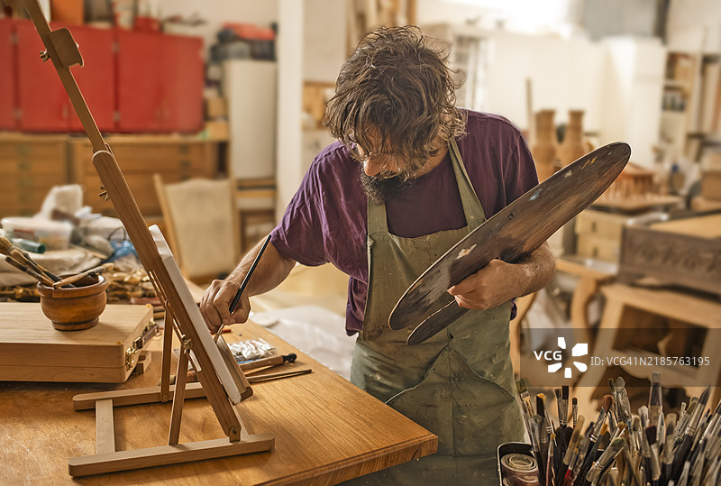 艺术家在艺术工作室中工作，前景是拿着调色板的画家图片素材