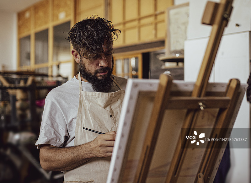 艺术家在艺术工作室中工作，前景是拿着调色板的画家图片素材