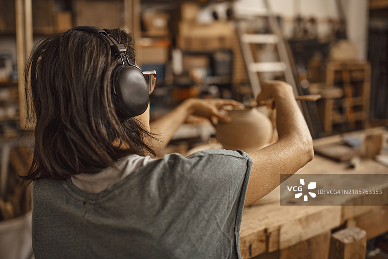 一位女性雕塑家在听着耳机音乐的同时捏制一块粘土图片素材