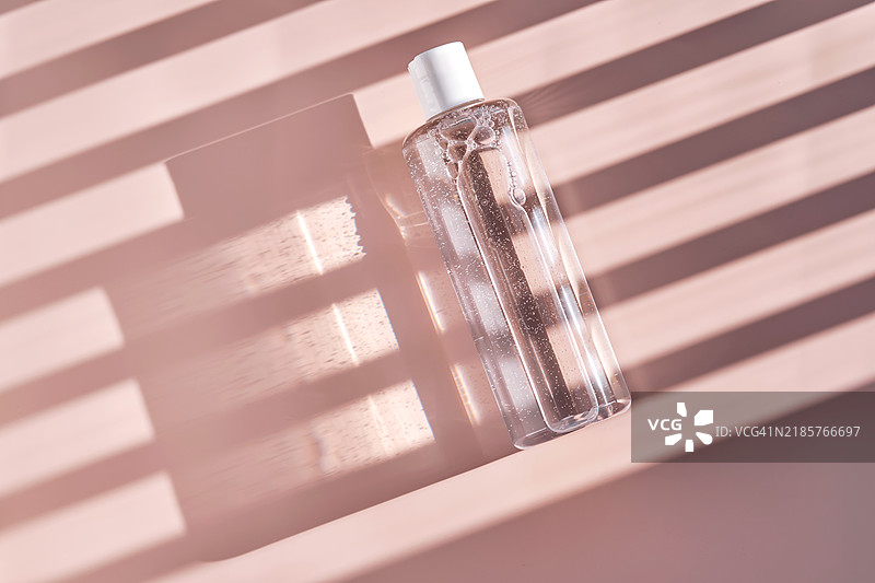 粉色背景上带有条纹阴影的面部爽肤水或洁面乳瓶图片素材