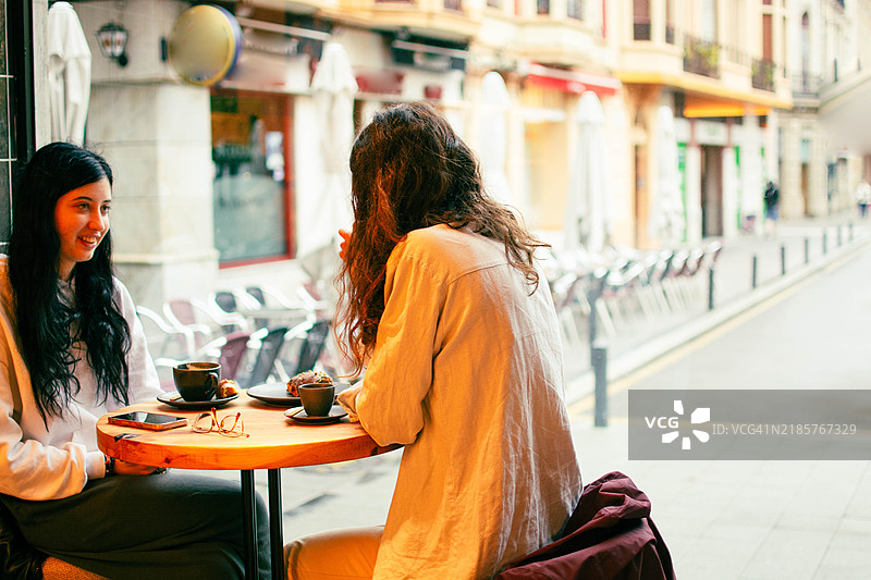 两个人坐在城市里一家舒适的咖啡馆的桌子旁。图片素材