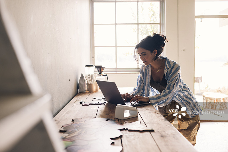 女性设计师在工作室的桌子上靠着工作，使用笔记本电脑。图片素材
