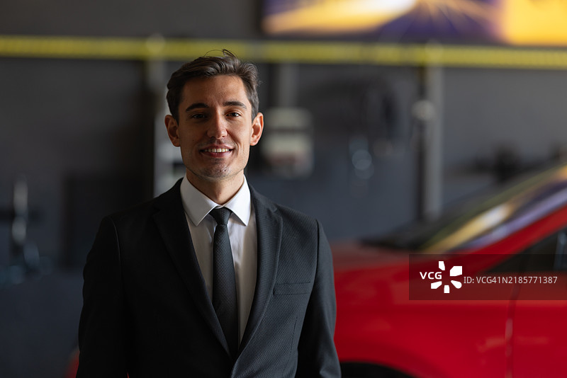 自信的商务专业人士在展厅旁摆姿势，身边是一辆红色汽车图片素材