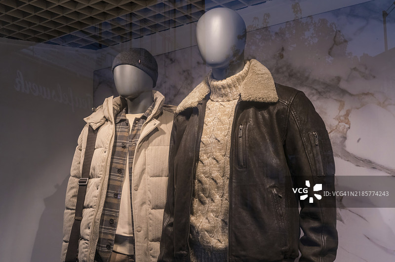 两个模特展示时尚的冬季外套和一件温暖的毛衣，展示了零售店环境中的当前潮流。图片素材