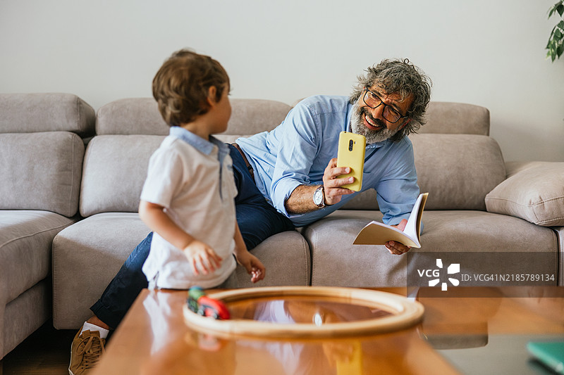 男人拿着手机给他的孙子拍照。图片素材