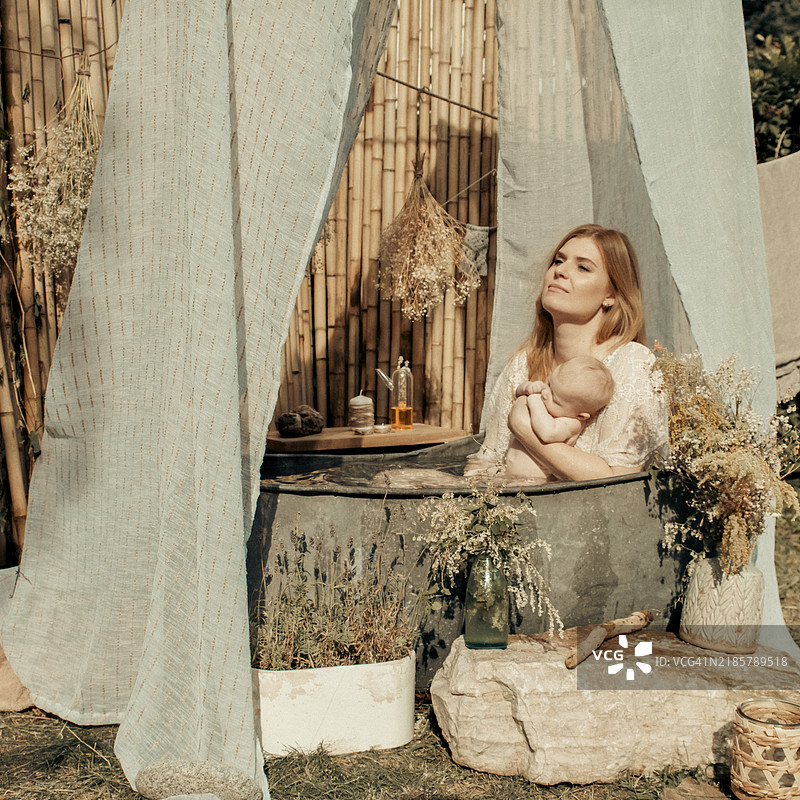 一位母亲和她的宝宝在花园里的锌浴缸中洗澡。图片素材