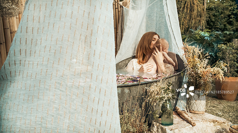 一位母亲和她的宝宝在花园里的锌浴缸中洗澡。图片素材