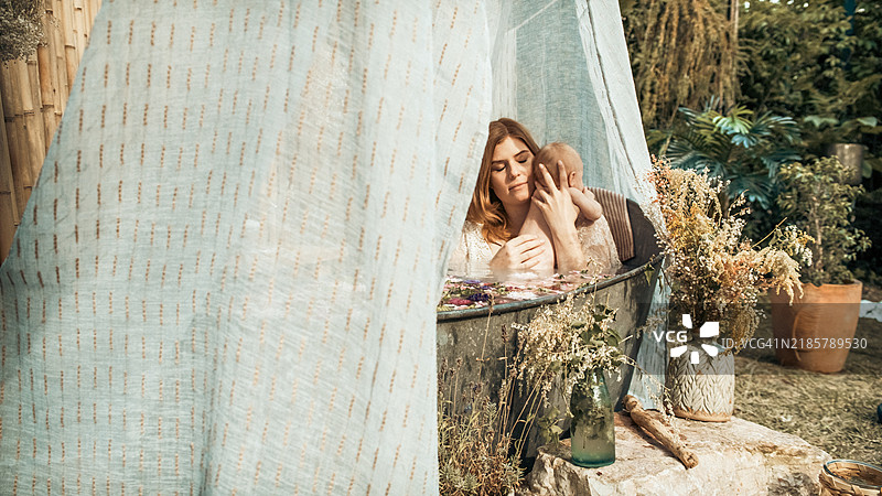 一位母亲和她的宝宝在花园里的锌浴缸中洗澡。图片素材