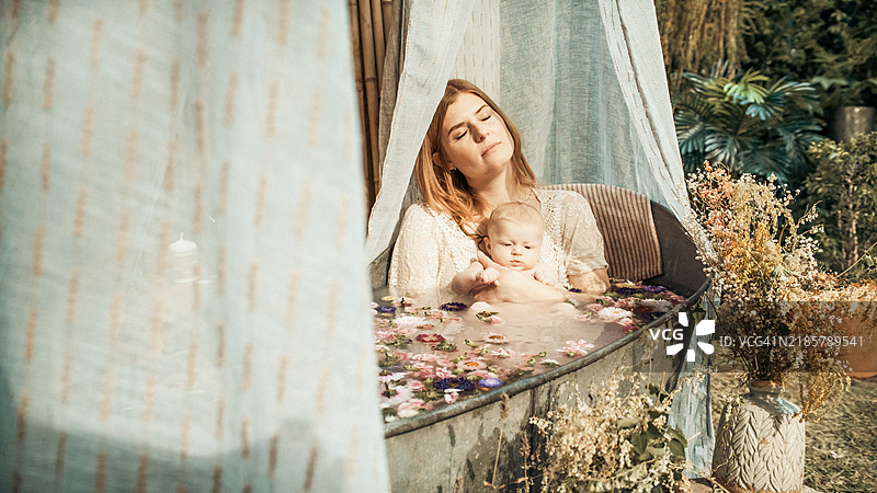 一位母亲和她的宝宝在花园里的锌浴缸中洗澡。图片素材