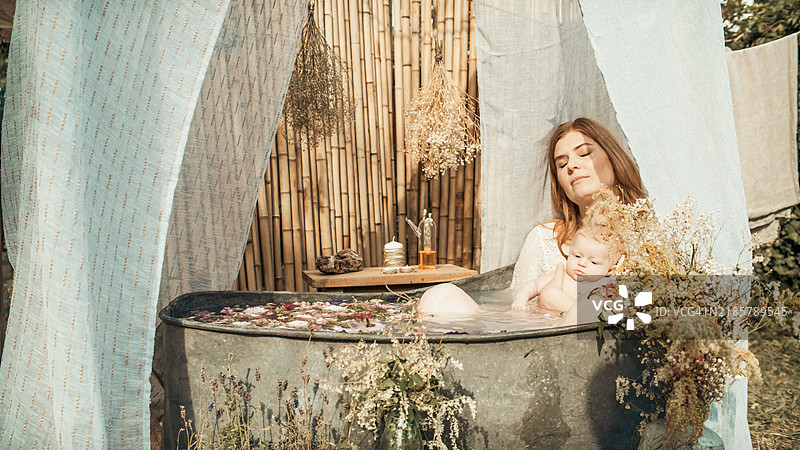 一位母亲和她的宝宝在花园里的锌浴缸中洗澡。图片素材