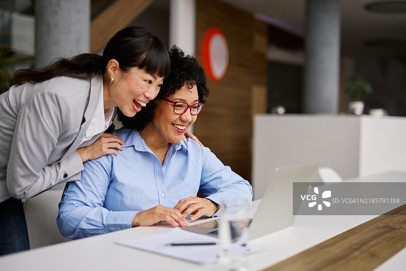 两位女性在现代办公室合作使用笔记本电脑图片素材