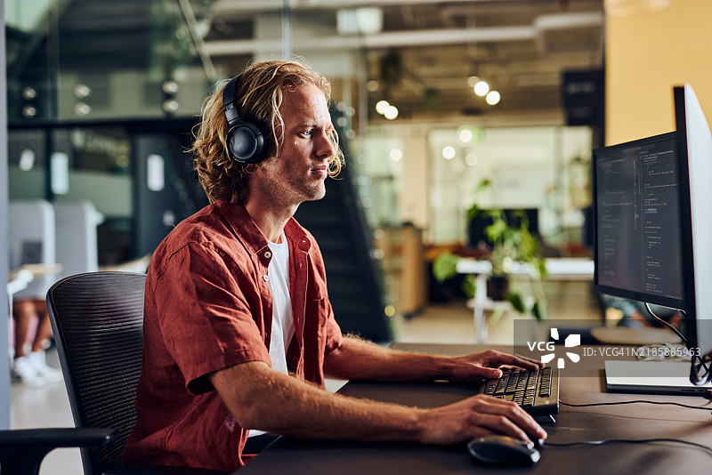 在现代办公室里，戴着耳机的计算机程序员正在编写人工智能代码图片素材
