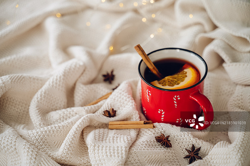 红色杯子里装着热的香料酒，旁边有橙子片、肉桂和八角，放在一条针织毛毯上。图片素材