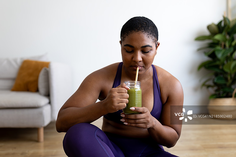 年轻女性在家锻炼后喝绿色果昔图片素材