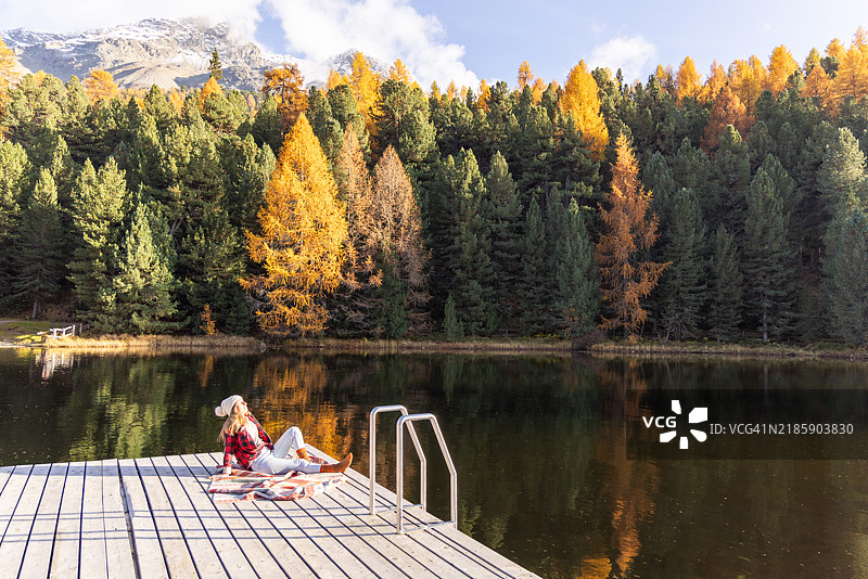 女人在充满活力的秋季风景中悠闲地坐在码头上图片素材
