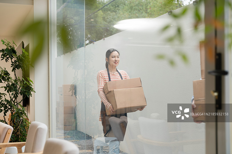 年轻的亚洲女性在新家搬箱子。图片素材