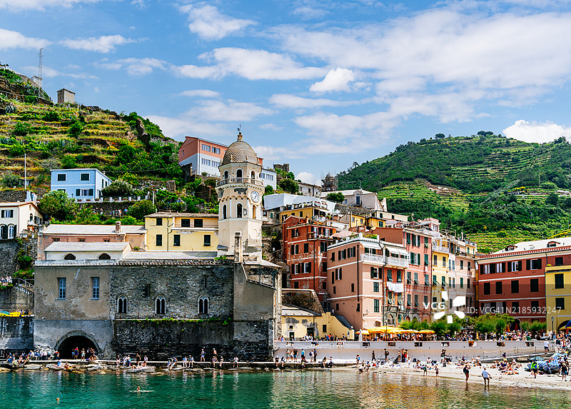风景如画的韦尔纳扎海滩和教堂，色彩斑斓的村庄建筑依偎在山坡背景上，俯瞰清澈的地中海水域。图片素材