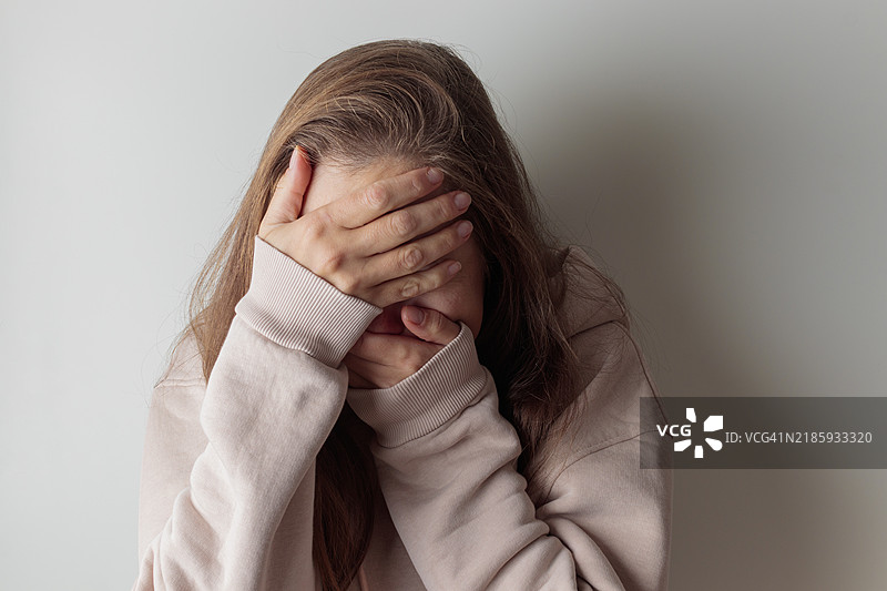 特写不快乐的年轻女性用双手掩面，感到绝望、被欺骗、无助和孤独，身处室内。图片素材
