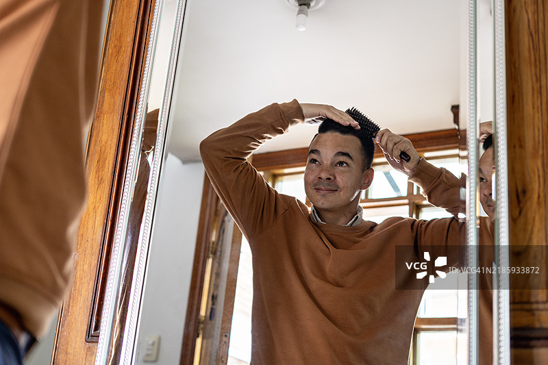 一个男人在家里对着镜子用梳子梳头。图片素材