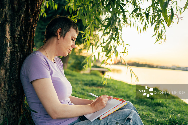 宁静的作家在黄金时刻享受自然的宁静，记录笔记并寻找灵感图片素材