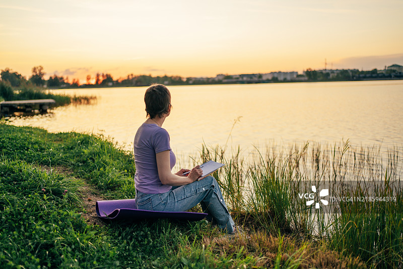 宁静的作家在黄金时刻享受自然的宁静，记录笔记并寻找灵感图片素材