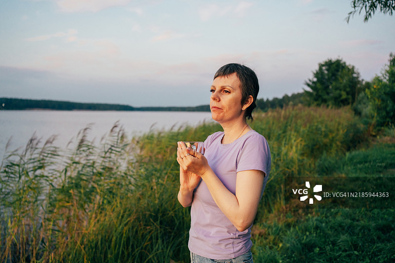 经历化疗后，短发的宁静女性凝视着平静湖面上的日落图片素材