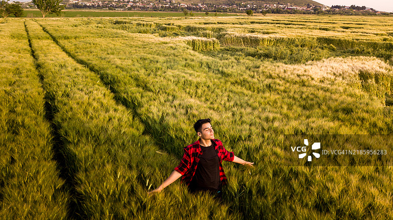 年轻男子在绿色麦田中张开双臂享受自由图片素材
