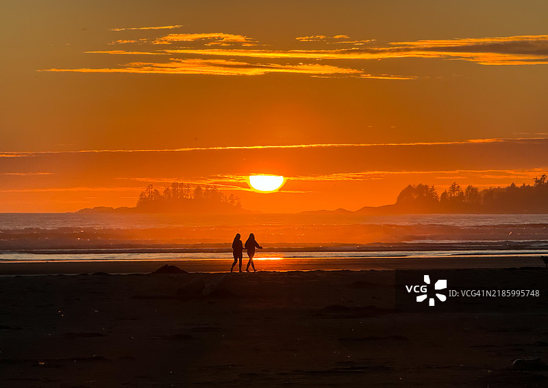 在加拿大不列颠哥伦比亚省的太平洋沿岸国家公园，黄昏时分，一对情侣在雾气弥漫的海滩上漫步的剪影。图片素材