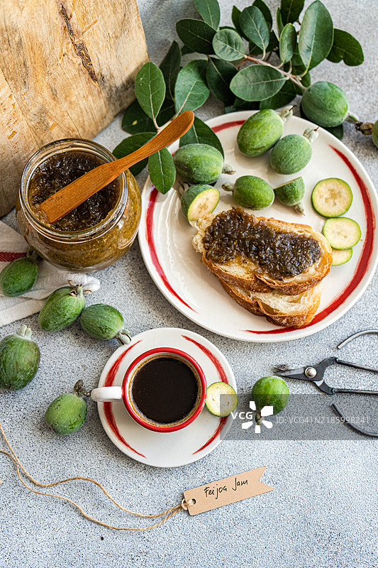 从上方俯视一杯黑咖啡和切片的白色酸面包，上面涂有费霍亚果酱，摆放在桌子上。图片素材