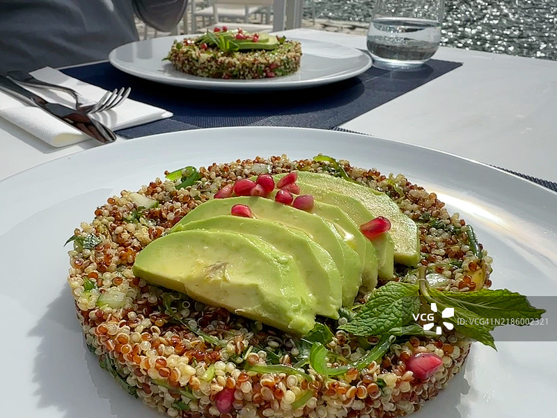 海边桌子上的两份藜麦沙拉特写，配有牛油果、石榴、开心果和薄荷图片素材