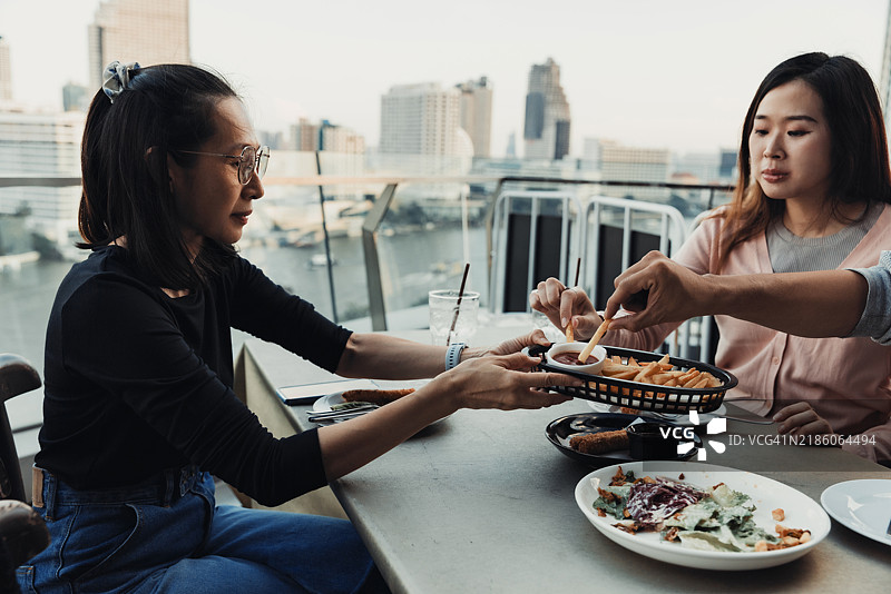 朋友们在日落时分的屋顶露台上共享美好餐点，俯瞰城市天际线。图片素材