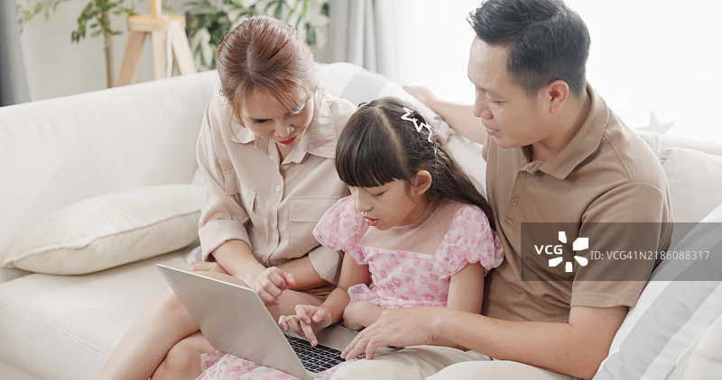 父母帮助女儿使用笔记本电脑学习。图片素材