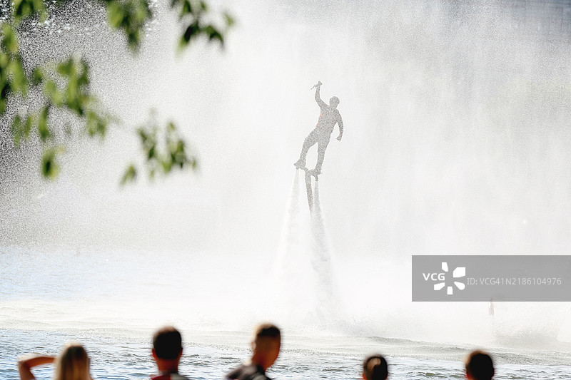 未知业余爱好者在模糊的湖面上展示飞板技能，背景是观众的剪影图片素材