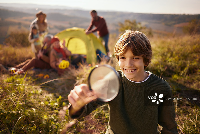 快乐的小探险者在秋天的露营日里使用放大镜。图片素材