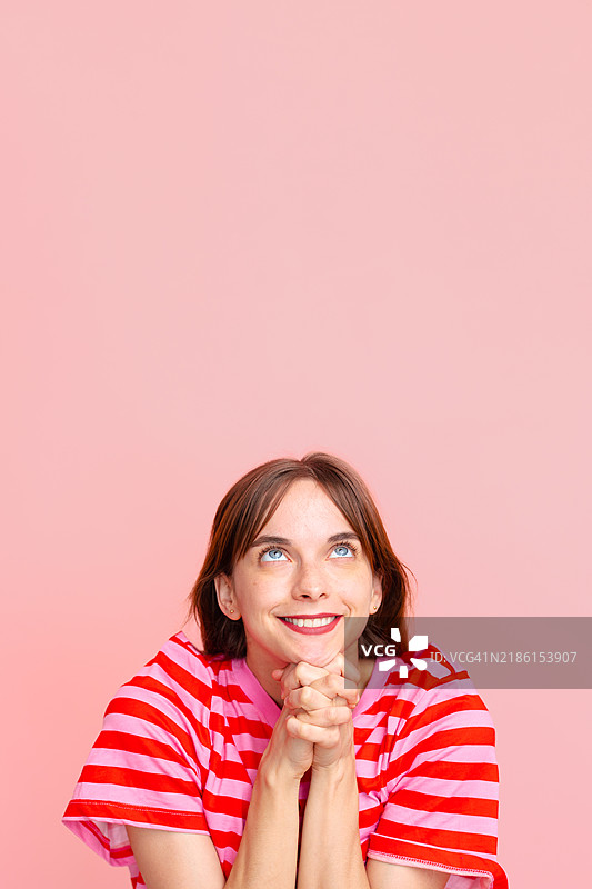 年轻女性在粉色背景下仰望，双手合十充满希望图片素材