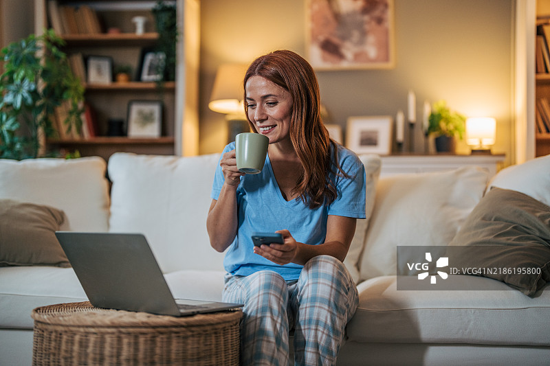一位快乐的成年女性穿着睡衣坐在客厅的沙发上。图片素材
