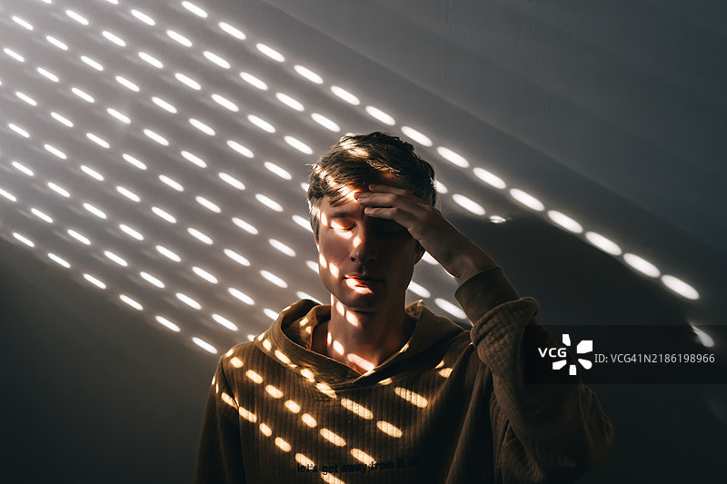 一位中年男子的脸上映射着百叶窗的光影，背景是灰色的墙壁。图片素材