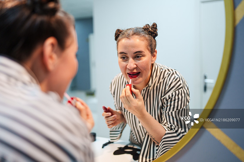 双丸子头的女性在镜子前涂口红。图片素材